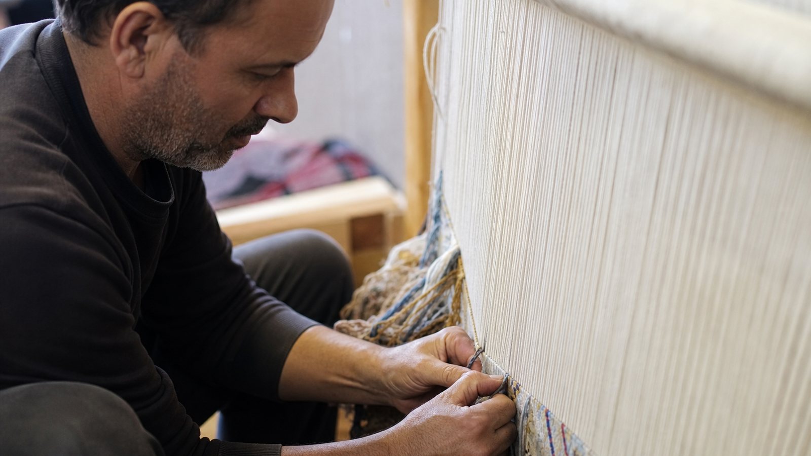 Artisan nouant a la main un tapis de laine sur un metier a tisser vertical traditionnel